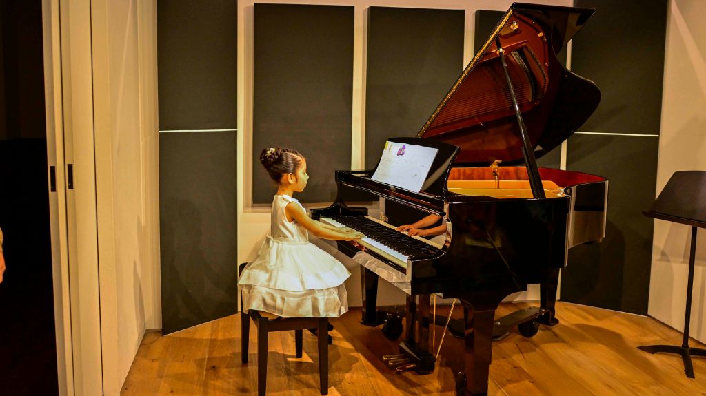 Young girl in a white dress sitting at a grand piano in a music studio during her spring recital.
